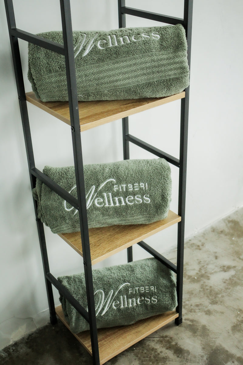 Green towels with 'Fitness Wellness' branding on a wooden shelf against a white wall.